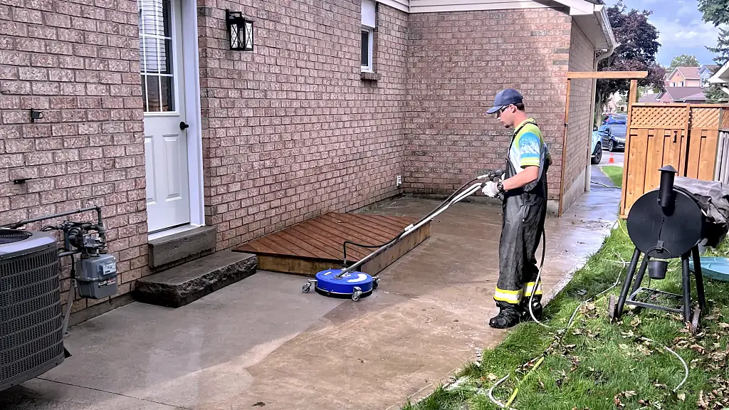 DSS technician surface-cleaning a concrete patio beside a brick home