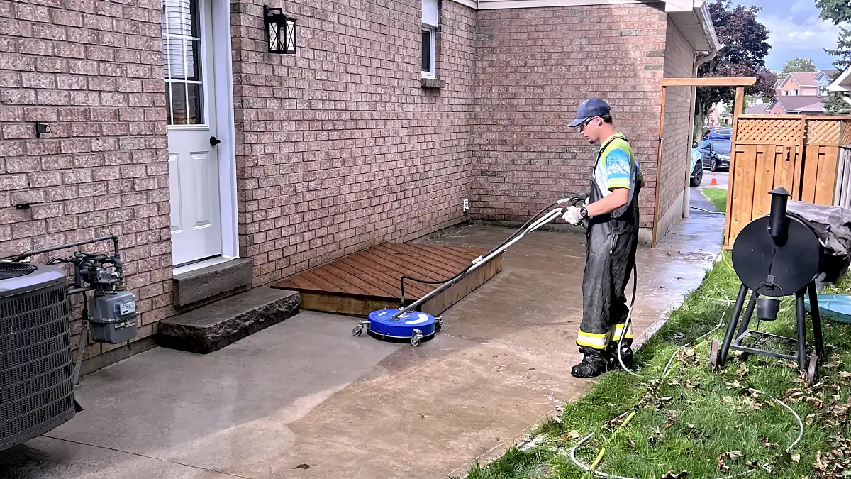 DSS technician surface-cleaning a concrete patio beside a brick home