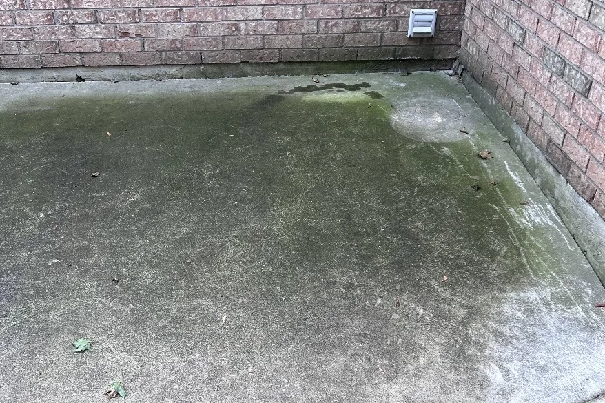 Before: Concrete pad beside a brick house covered in green algae and dirt
