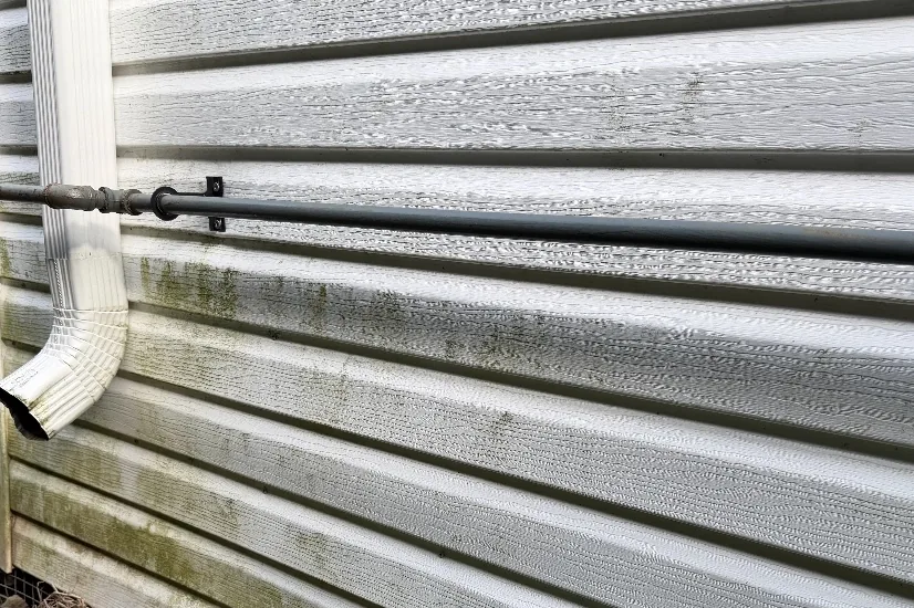 Before: Grey vinyl siding at a downspout corner with dark mildew